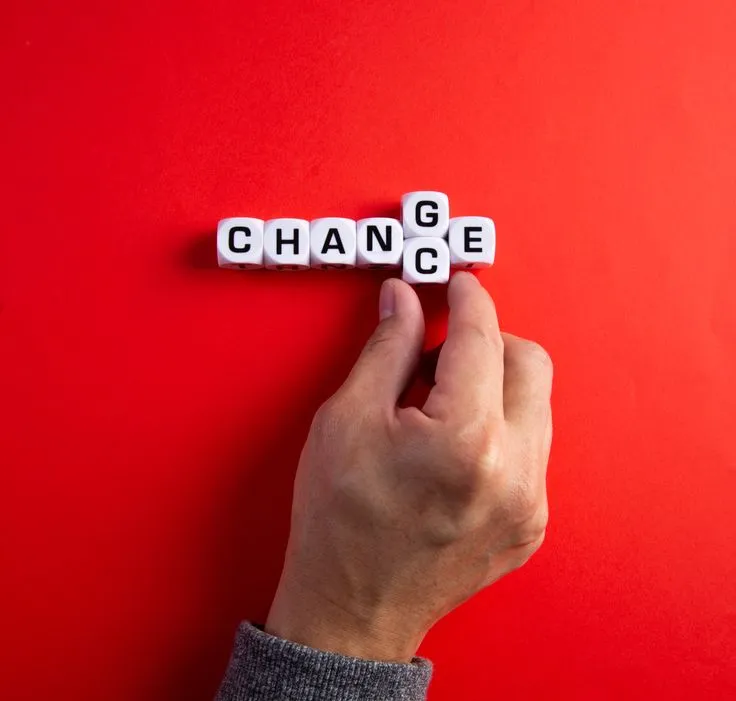 Hand dreht einen Buchstabenwürfel, sodass aus „Change“ das Wort „Chance“ wird, auf rotem Hintergrund