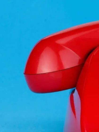 Nahaufnahme eines roten Telefonhörers auf einem Retro-Telefon vor blauem Hintergrund