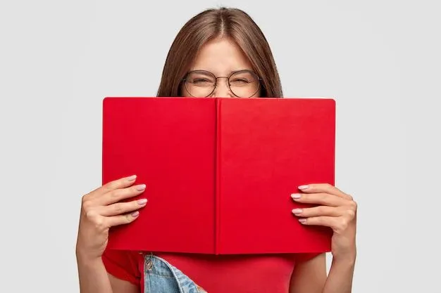 Lächelnde junge Frau mit runder Brille hält ein aufgeschlagenes rotes Buch vor ihr Gesicht, heller Hintergrund